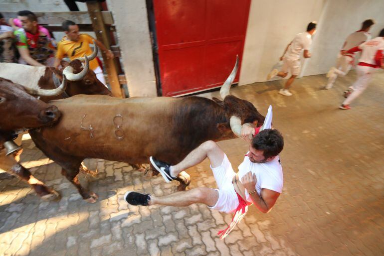 Encierro de Sanfermines. Corredor colgando por el pañuelo de un miura.