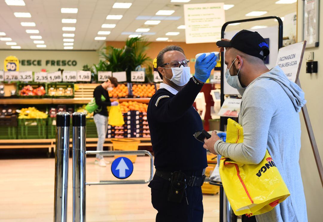 Un empleado de seguridad toma la temperatura a un hombre con mascarilla a la entrada de un supermercado en Turin