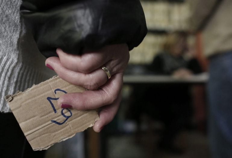 Una mujer espera para recibir una bolsa con comida en un banco de alimentos de Atenas