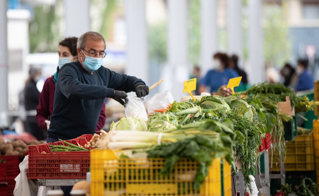 Un hombre con mascarilla despacha verduras en un mercado agrícola.