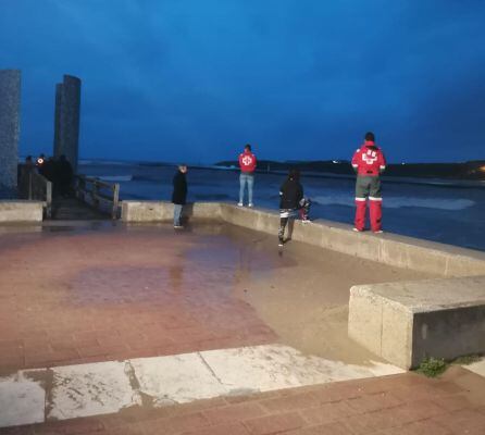 Miembros de los equipos de rescate buscan a la persona arrastrada por una ola en la barra de Suances.