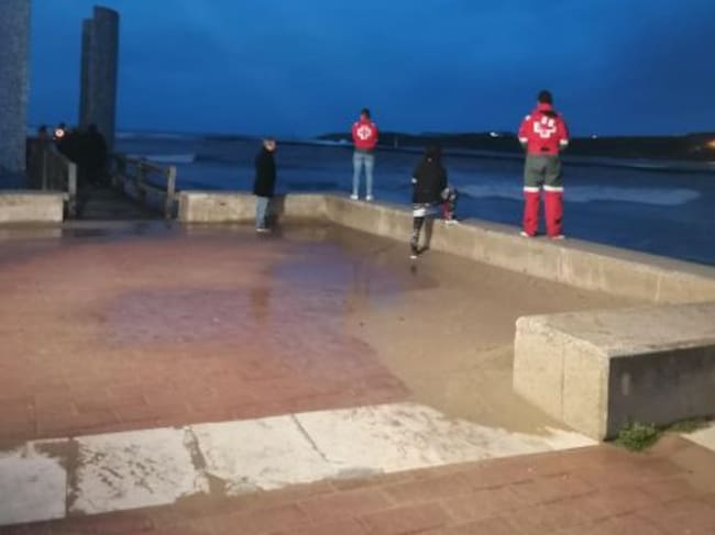 Miembros de los equipos de rescate buscan a la persona arrastrada por una ola en la barra de Suances.