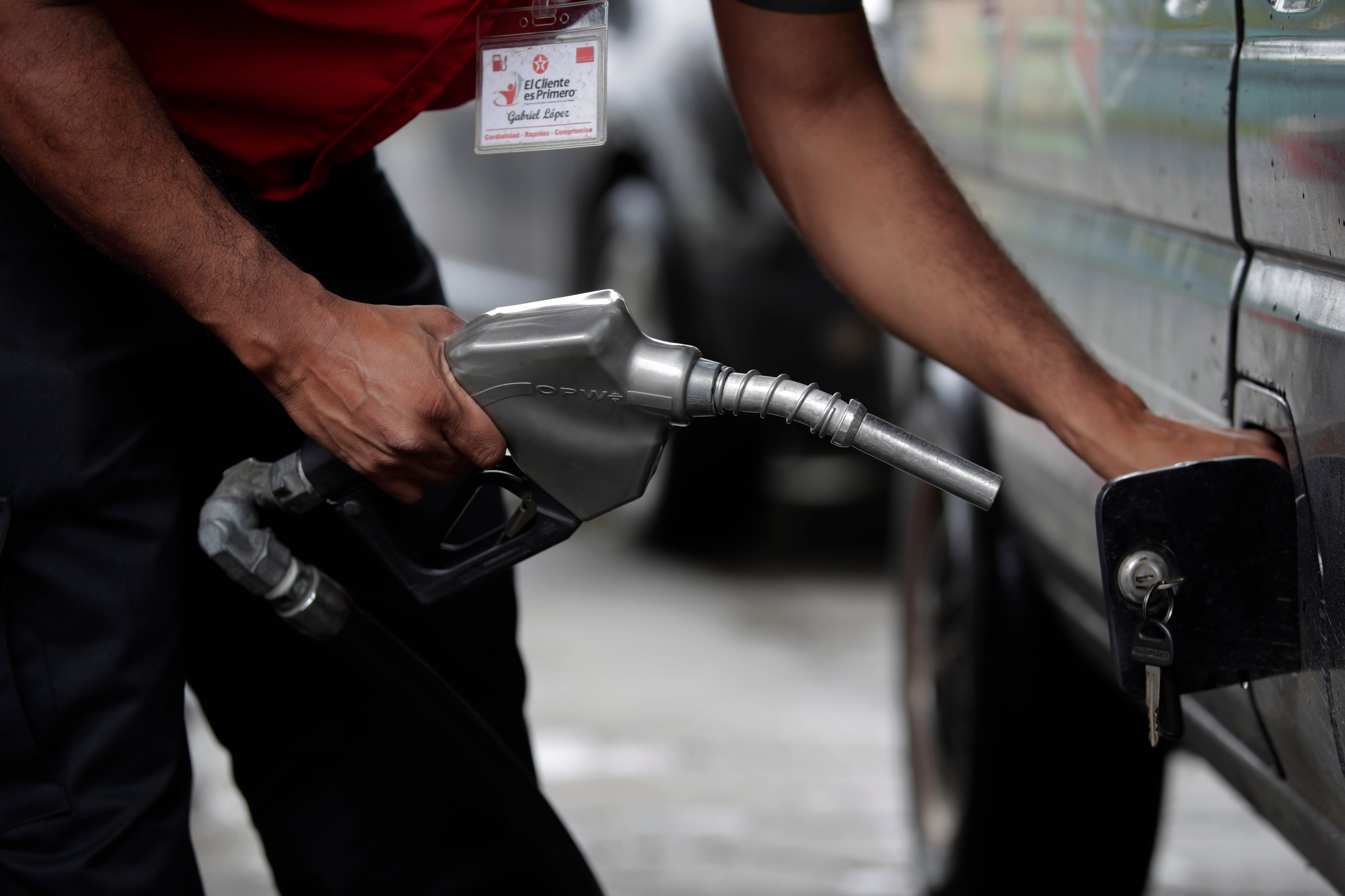 Un empleado de una gasolinera vierte gasolina en un vehículo.