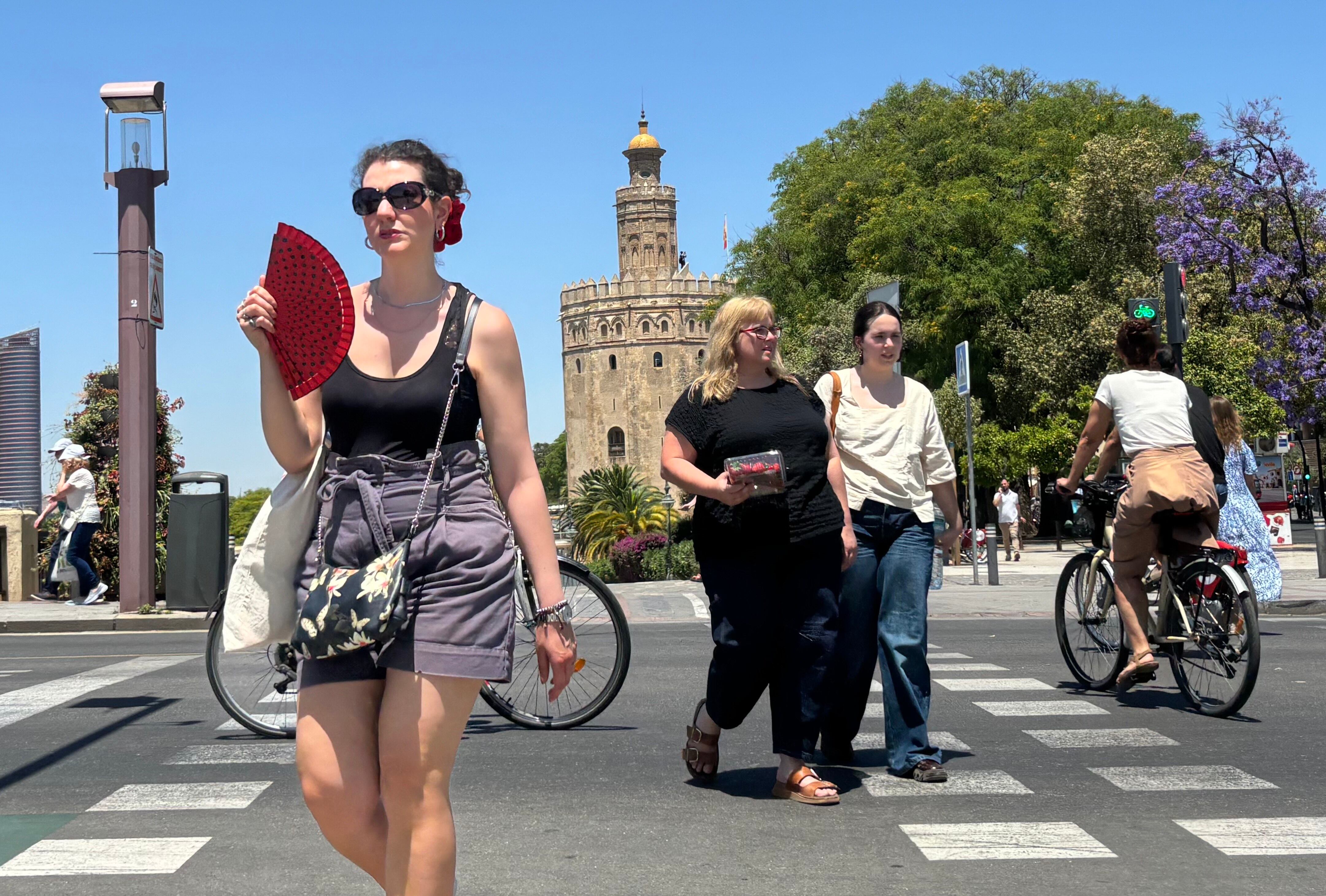 Varias personas caminan cerca de la Torre del Oro de Sevilla.
