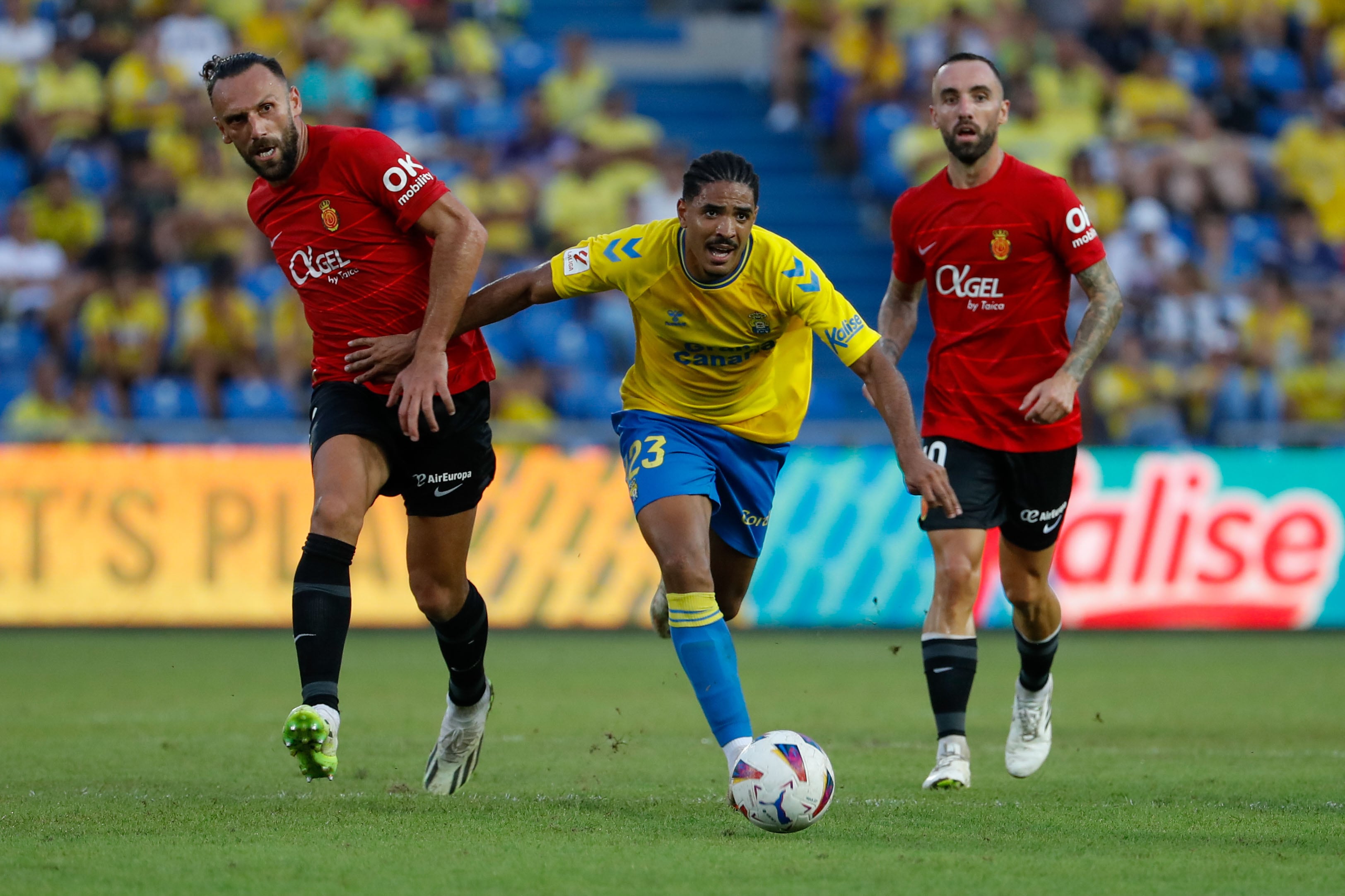 GRAFCAN5569. LAS PALMAS DE GRAN CANARIA, 12/08/2023.- El jugador de la UD Las Palmas Coco (c) y los jugadores del RCD Mallorca Muriqi (i) y Darder (d) durante el partido de la primera jornada de la Primera División que ambos equipos disputaron este sábado en el Estadio de Gran Canaria. EFE/ Elvira Urquijo A.
