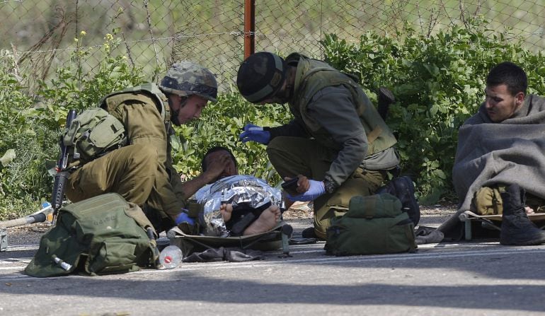 Un soldado isrelí herido recibe atención médica de varios compañeros después de que impactara un misil antitanques en su vehículo en la frontera entre Israel y el Líbano.