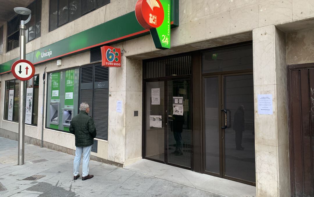 Una persona lee un cartel ante las puertas de una oficina de Unicaja cerrada en la capital.