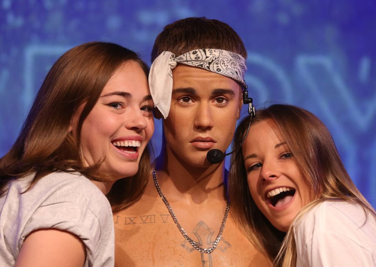 Dos fans sonríen mientras posan con la figura de Justin Bieber, que luce tatuajes.