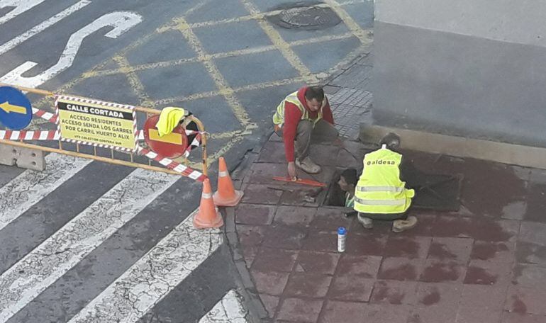 Trabajadores de Aldesa se introducen por un pozo de registro para medir la distancia entre la pasarela peatonal y las acequias subterráneas