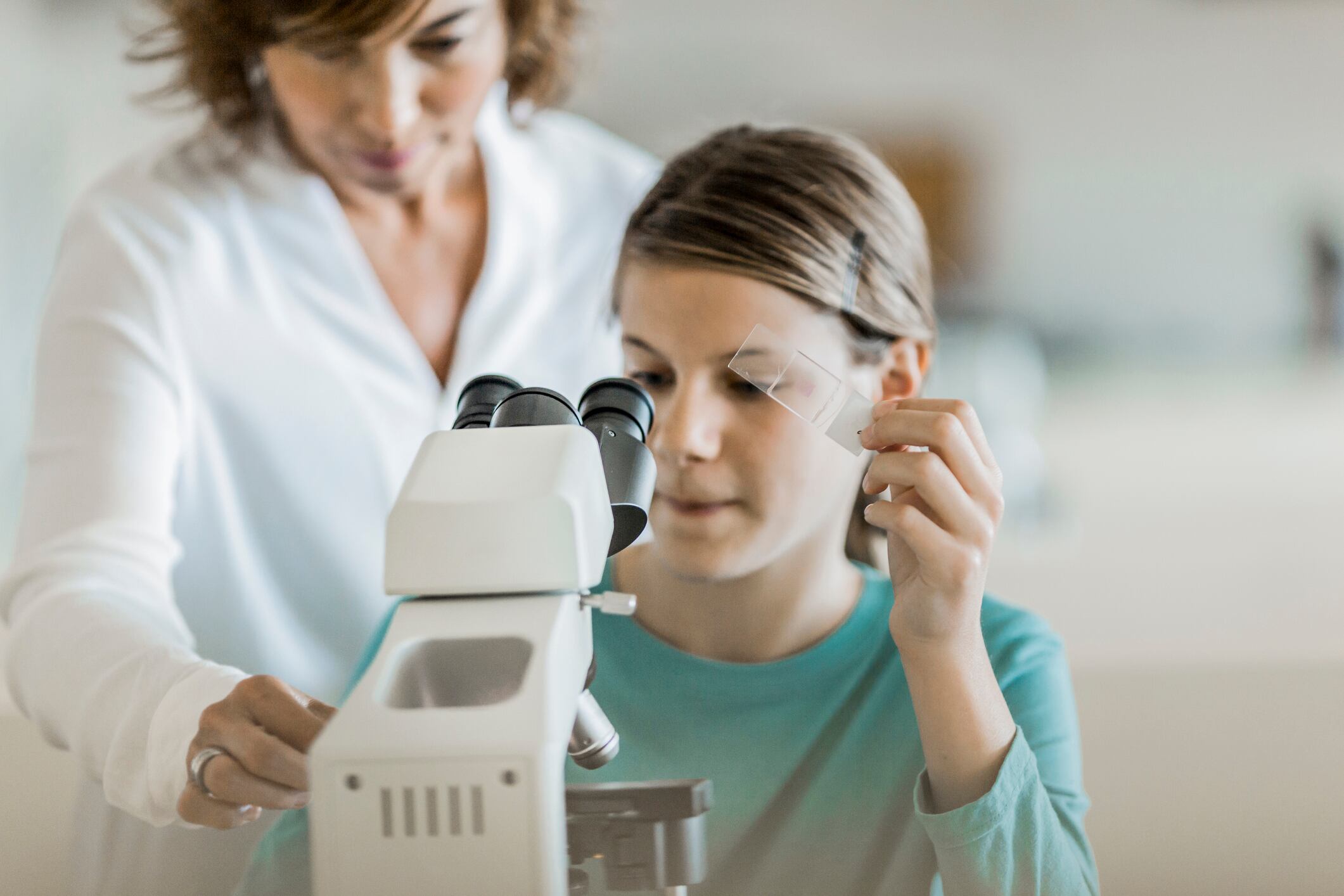 Una profesora y su alumna junto a un microscopio