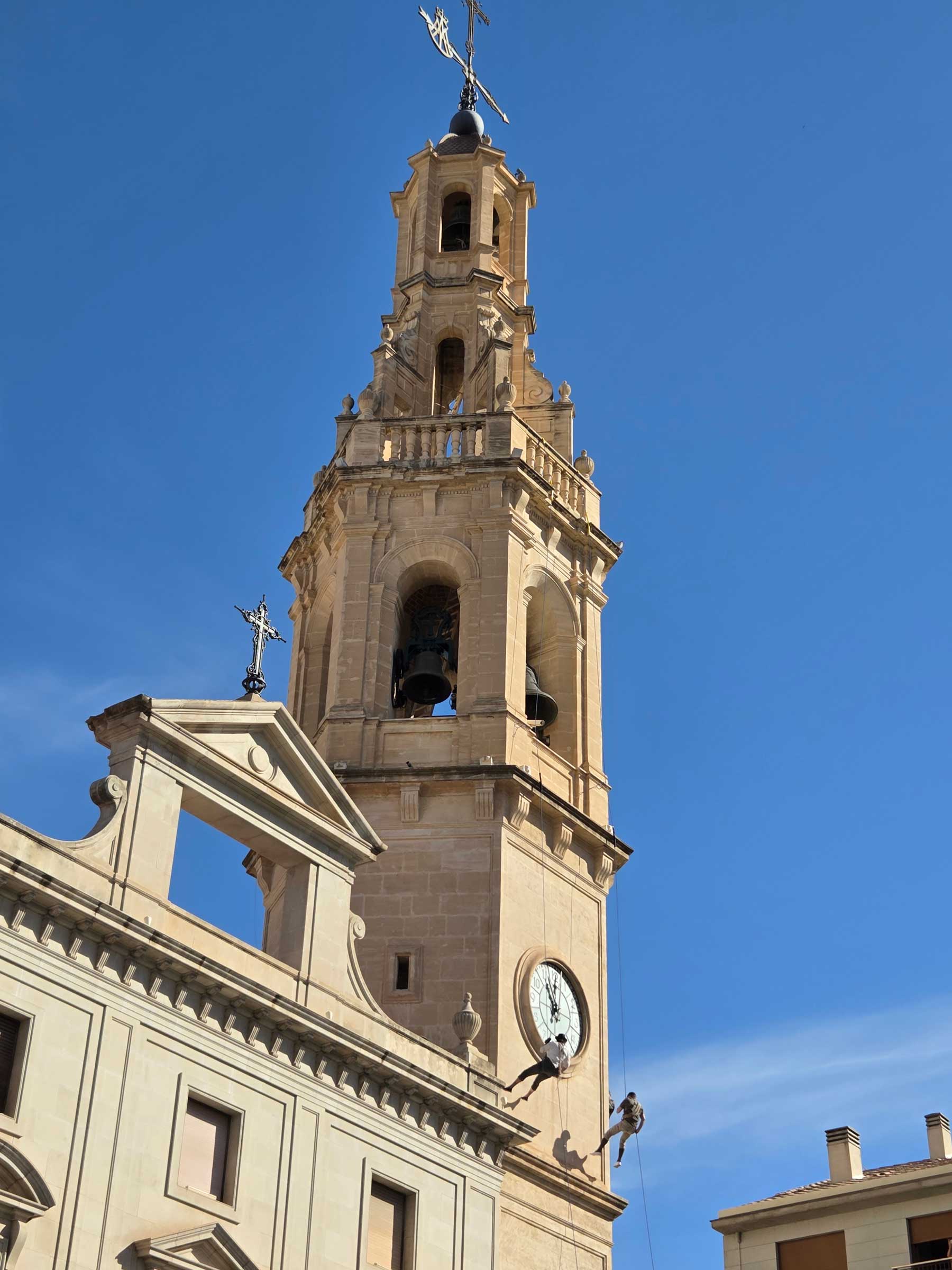 Dos de los componentes de la sección de alpinismo y escalada del Centre Excursionista Alcoi deslizándose por el campanario de Santa María vestidos de la época