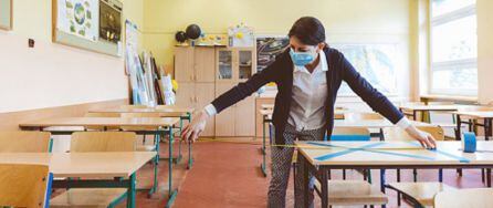 Docente midiendo la distancia entre pupitres en un aula escolar