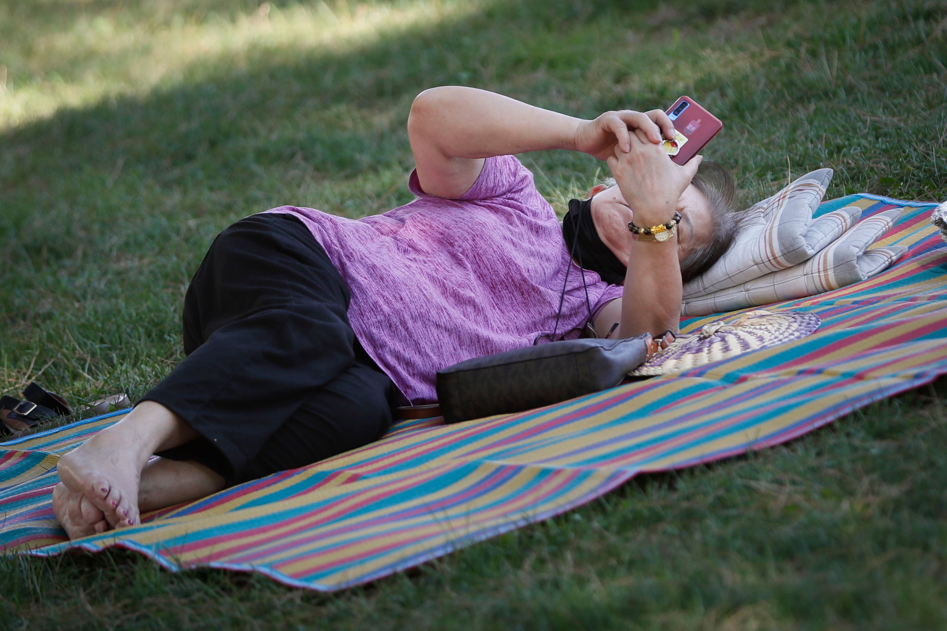 MADRID, 07/08/2022.- Una mujer descansa sobre el césped del Parque del Oeste, en Madrid, este domingo. La primera semana de agosto se despide con una jornada de cielos despejados en la mayoría del país y temperaturas que, si bien no son extremas, sí son elevadas, con termómetros que marcarán máximas de 36-39 grados en amplias zonas del interior peninsular y los 32-37 grados en el Mediterráneo. EFE/ Mariscal
