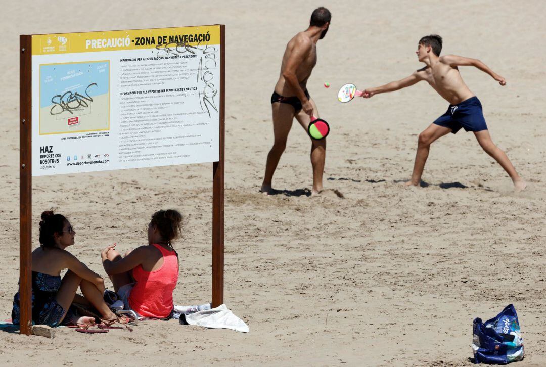 Dos mujeres se protegen del sol a la sombra de un cartel en la playa de la Malvarrosa. 