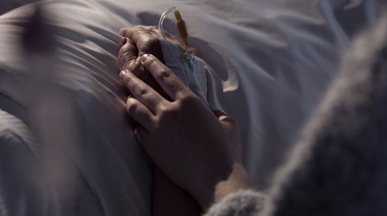 Imagen de una persona mayor ingresada en un hospital y de un familiar que le coge la mano.