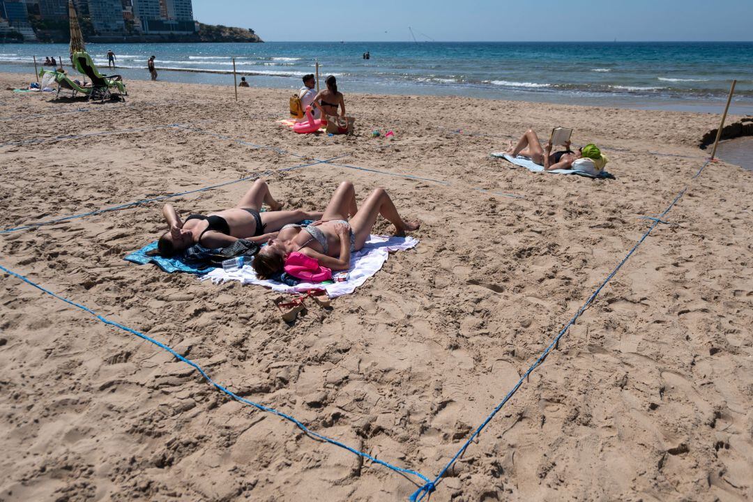 Varias personas toman el sol en la playa de Poniente de Benidorm, que este año ha tenido que parcelar su arenal para garantizar que se cumple la distancia de seguridad. 