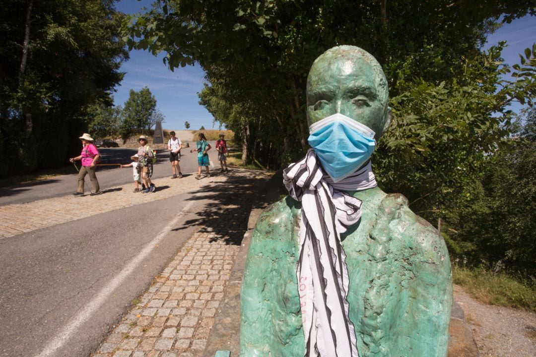 Un grupo de peregrinos llega a O Cebreiro pasando junto a la escultura del coruñés Miguel Couto, que luce desde hace semanas una mascarilla quirúrgica en recuerdo de las víctimas del Covid-19, mientras los peregrinos retornan al Camino francés de la Ruta Jacobea casi un mes después del fin del estado de alarma por el coronavirus, en O Cebreiro, Lugo, Galicia (España), a 15 de julio de 2020