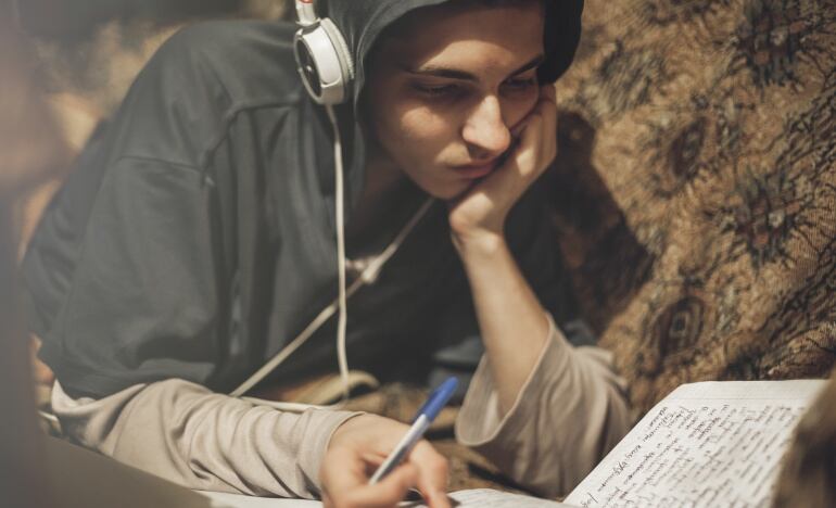 Imagen de un chico escribiendo en un cuaderno mientras escucha música con unos cascos.