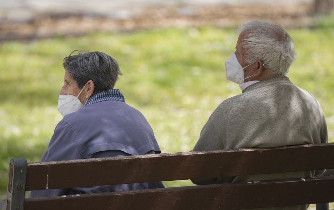 Un hombre y una mujer mayores, sentados en un banco y con mascarilla, en el Parque del Manzanares