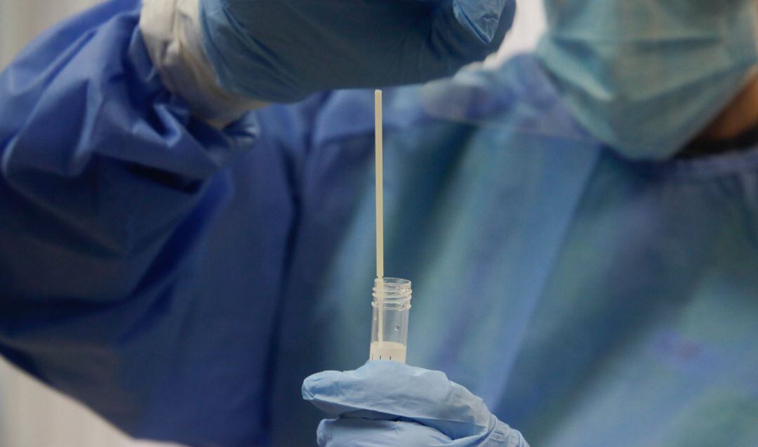 Una trabajadora sanitaria sostiene una probeta con una prueba PCR