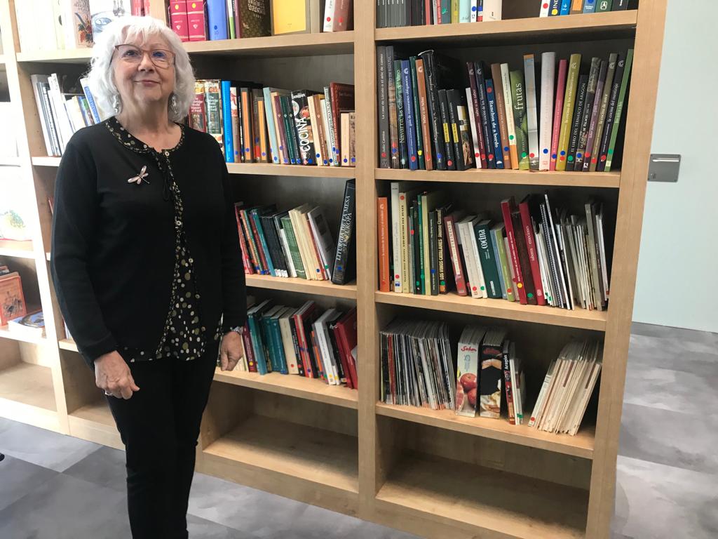 Elena Piedrafita, bibliotecaria de la Academia Aragonesa de Gastronomía, junto a los libros donados en un par de estanterías de la Biblioteca del Centro de Innovación Gastronómica