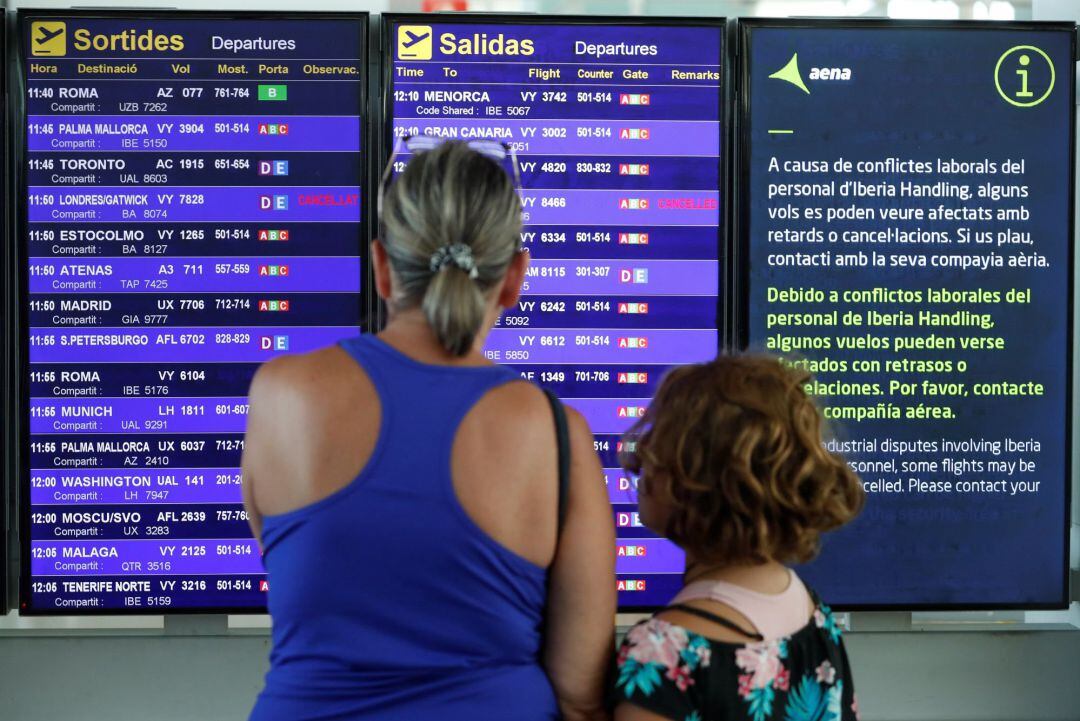 Una mujer y su hija consultan los paneles de saludas del aeropuerto del Prat