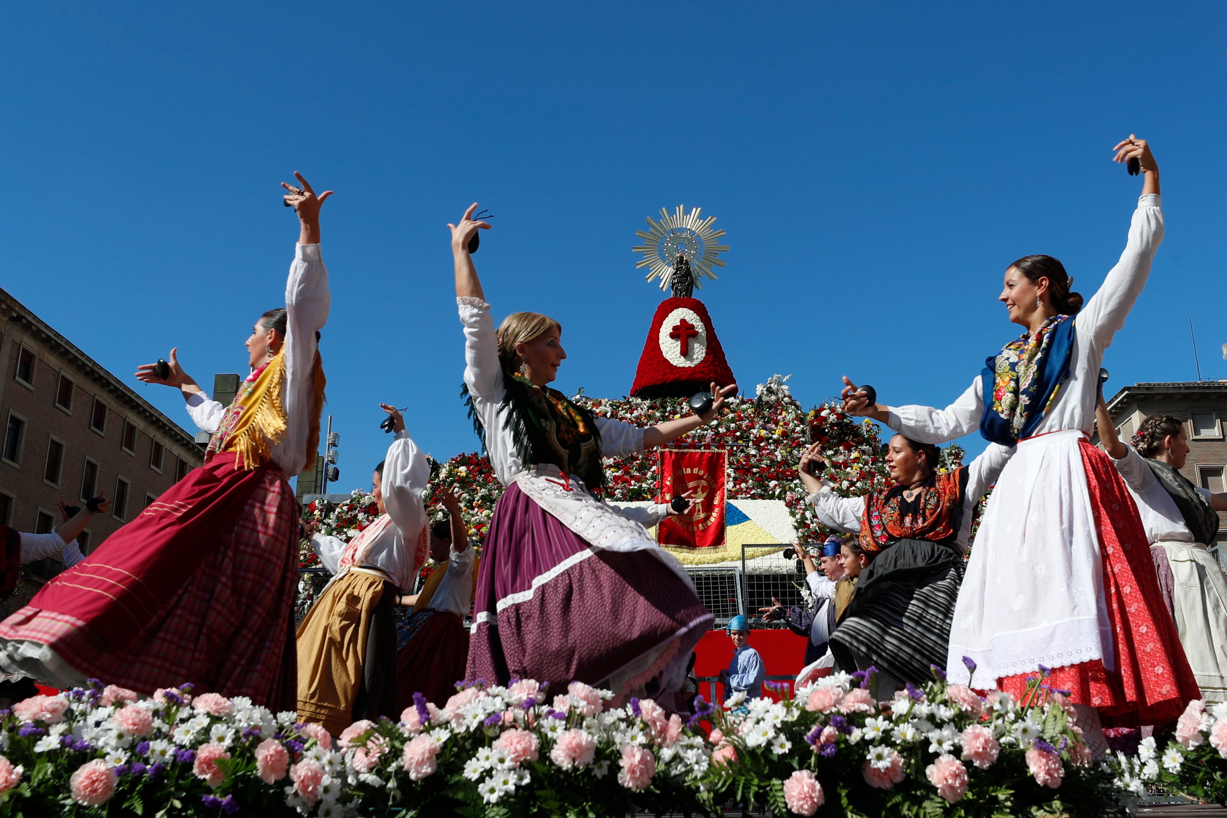 ZARAGOZA, 12/10/2022.- Varias personas bailan junto a la imagen de la Virgen del Pilar que luce ya las primeras flores en una estructura levantada en el centro de la plaza de Zaragoza que lleva su nombre, una ofrenda llena de ilusión que se espera de récord tras dos años de pandemia, con más grupos inscritos que en 2019 y la previsión de alcanzar alrededor de siete millones de flores. EFE/ Javier Cebollada
