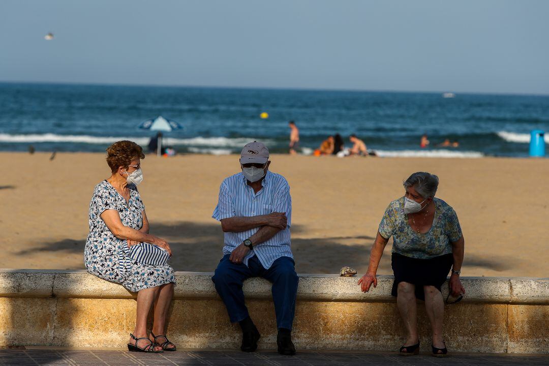 Tres personas mayores descansan en el paseo marítimo de València