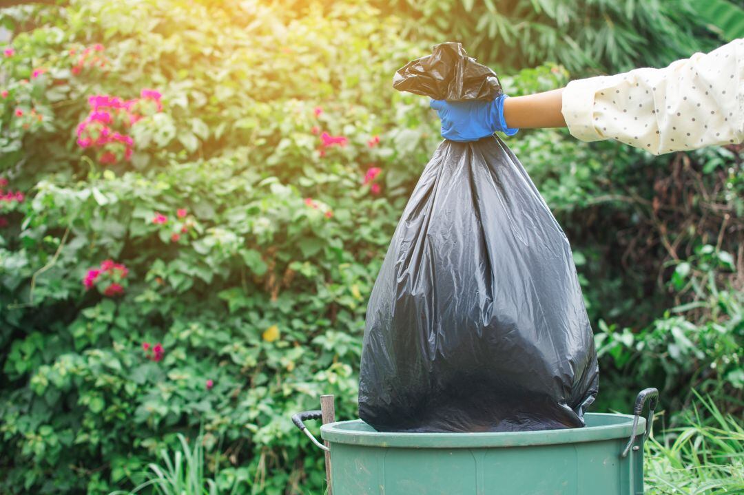 Una persona deposita una bolsa de basura en un cubo.