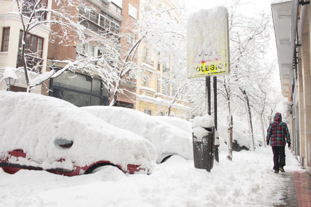 Una persona pasea por una céntrica calle cubierta de nieve junto al acceso de un colegio en Madrid.