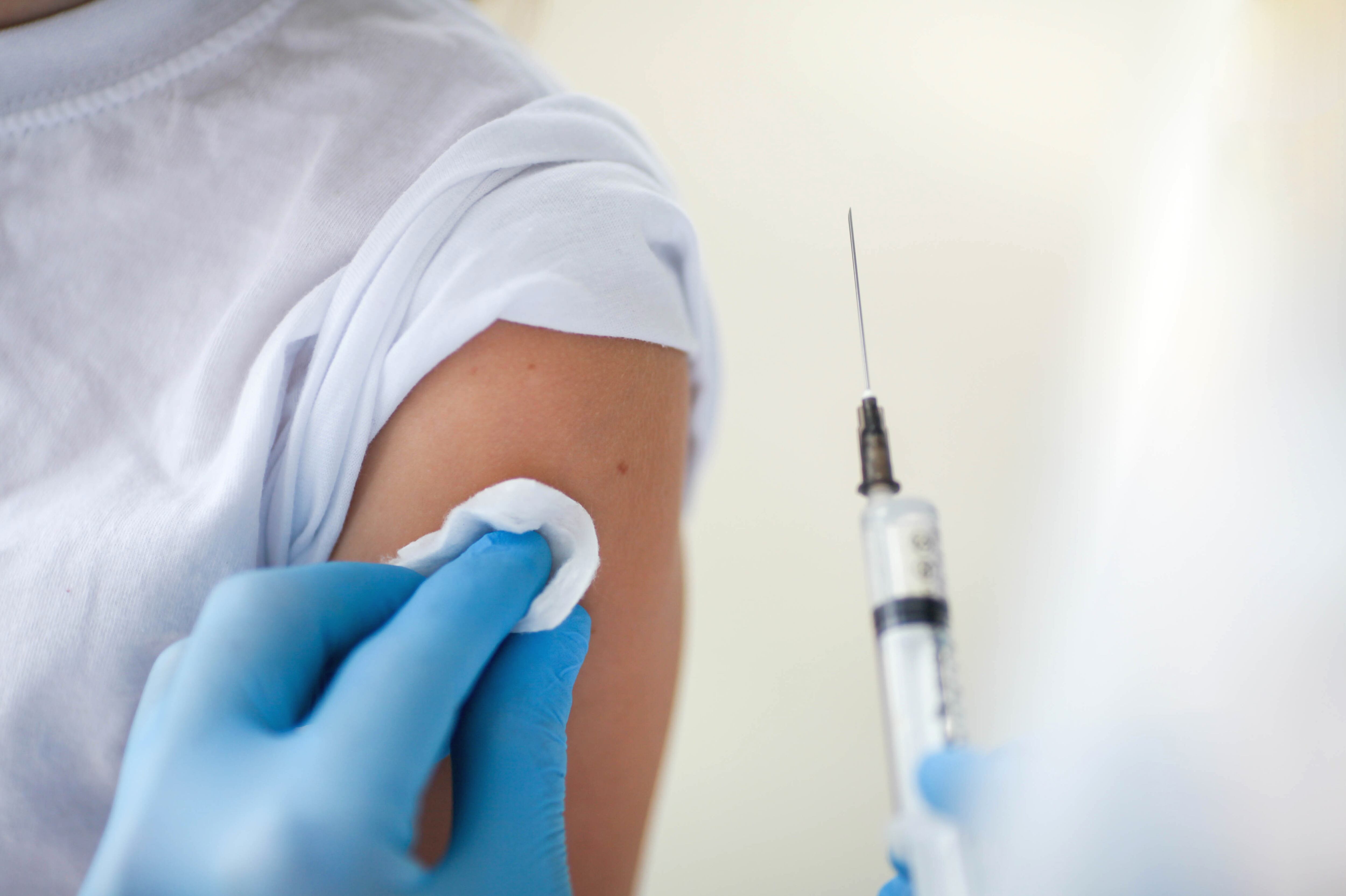 Close-up of a child is shoulder and the hands of a doctor in medical gloves with an injection for vaccination. Vaccination against coronavirus covid-19.