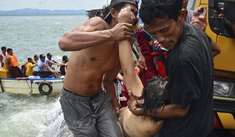 Varias personas sacan el cadáver de uno de los pasajeros del agua durante las labores de búsqueda y rescate de víctimas junto a la embarcación que naufragó en aguas frente al puerto de Ormoc, en el centro de Filipinas.