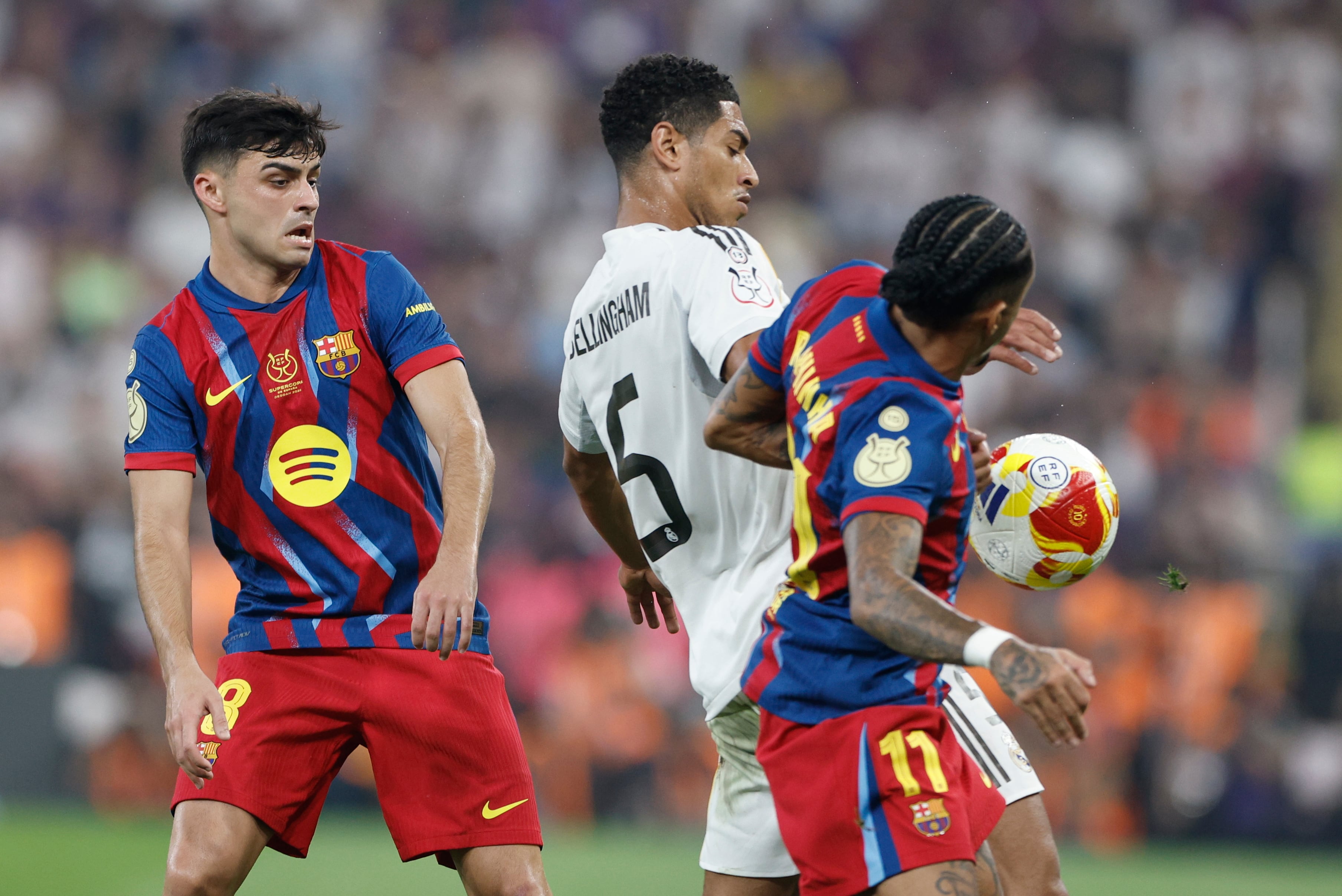 YEDA (ARABIA SAUDÍ), 11/01/2026.- Los jugadores del FC Barcelona Pedri (i) y Raphinha (d) disputan un balón con el centrocampista del Real Madrid Jude Bellingham (c) durante la final de la Supercopa de España entre el FC Barcelona y el Real Madrid, este domingo en el estadio Ciudad Deportiva del Rey Abdalá de Yeda (Arabia Saudí). EFE/ Kai Försterling