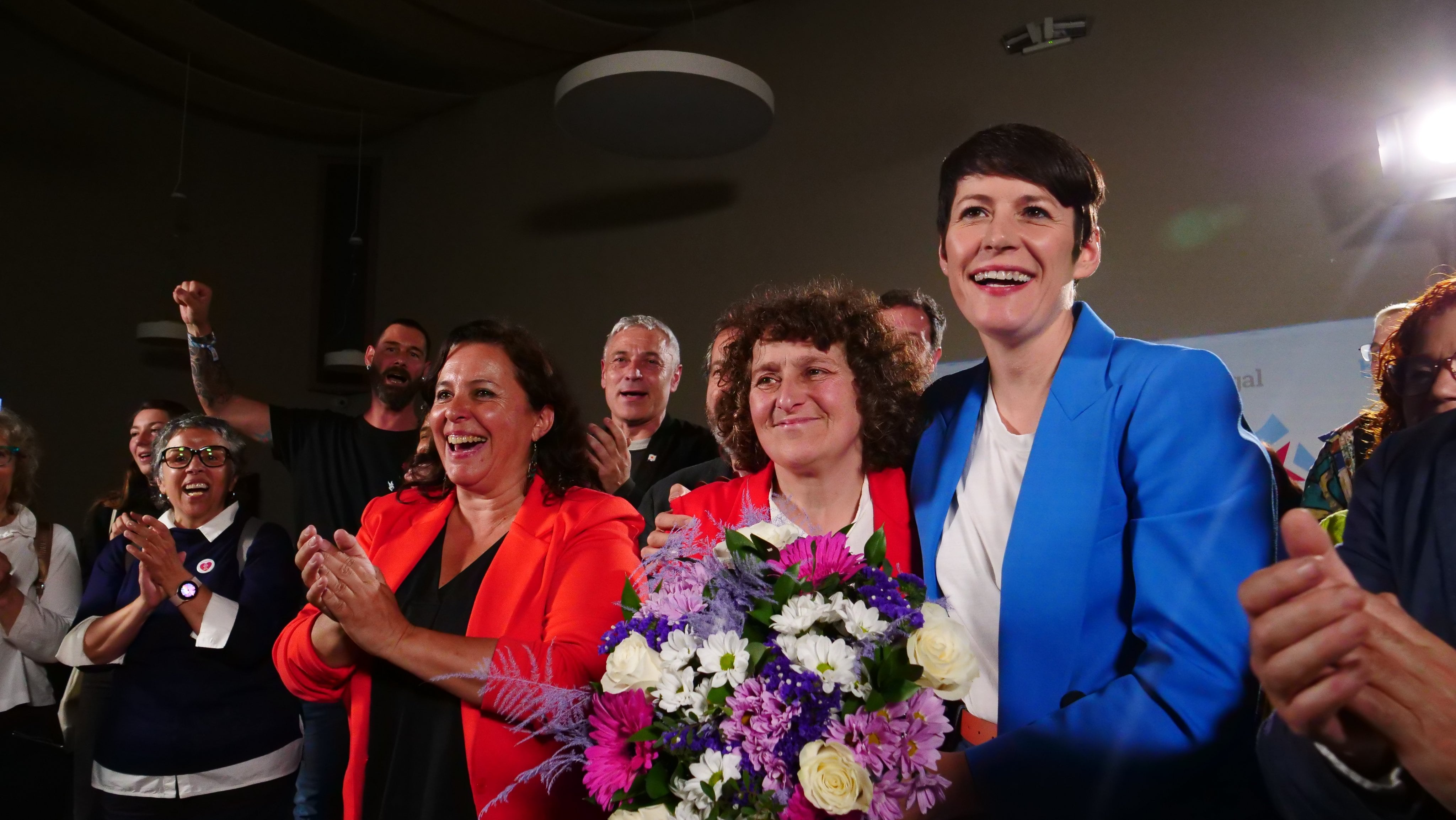 Goretti Sanmartín, sonriente en el centro de la imagen sostiene un ramo de flores, mientras se abraza con Ana Pontón