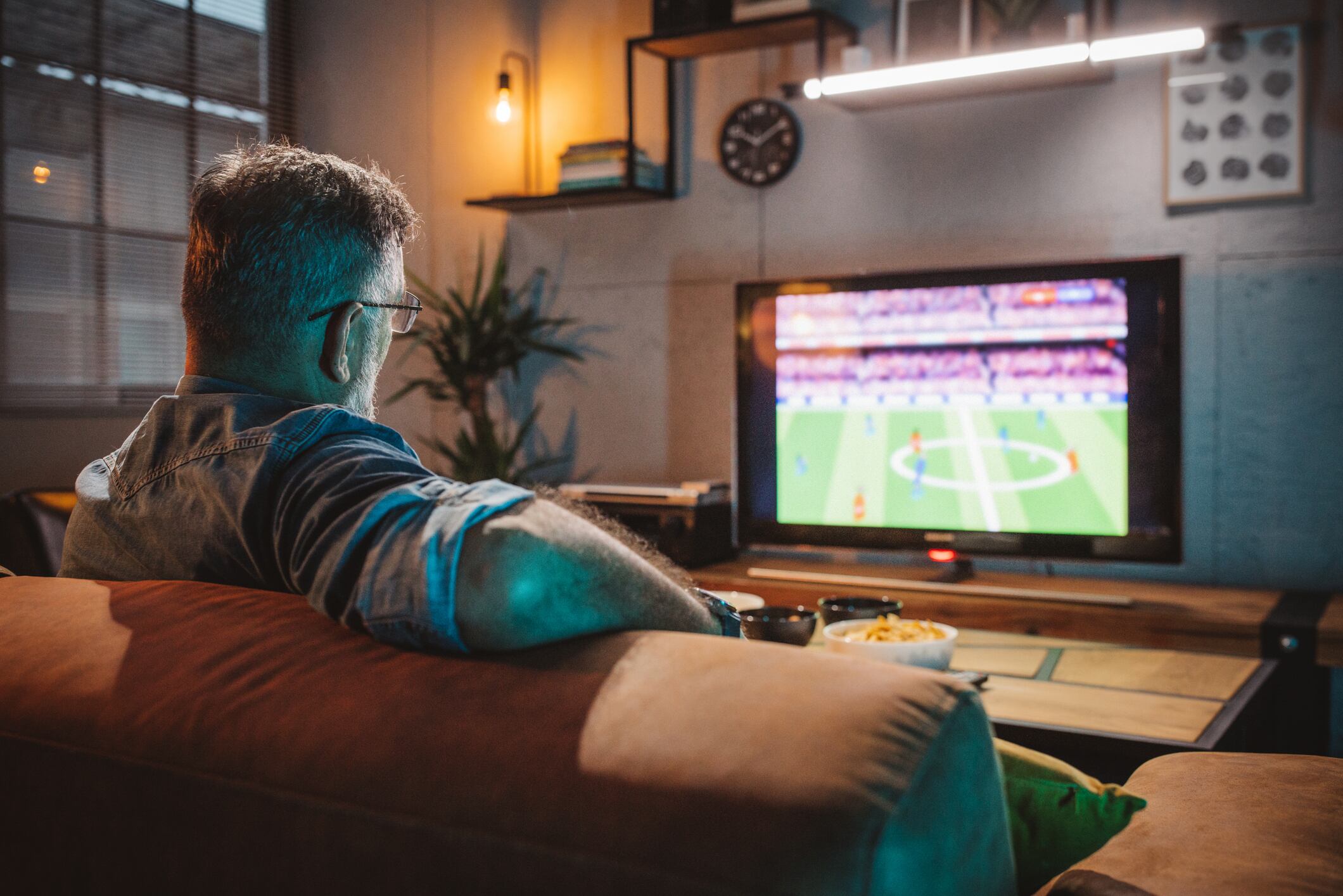 Mature men sitting on sofa at home and watching soccer game. He is cheering for favorite soccer team.