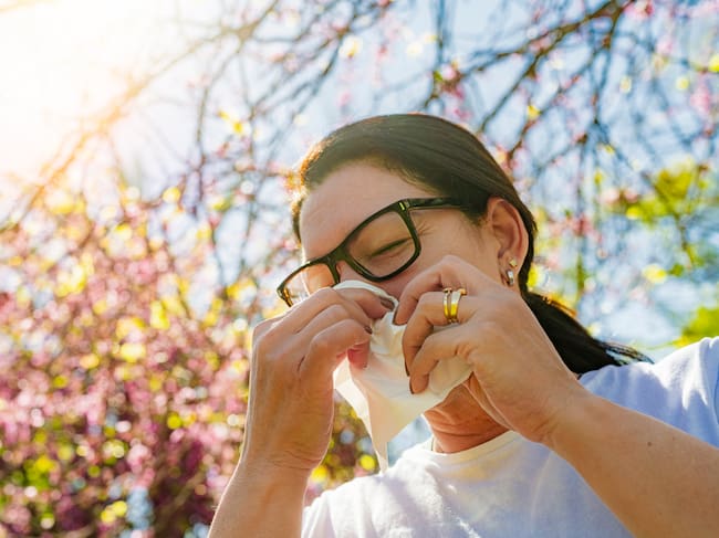 Una mujer al sol con alergia al polen se suena la nariz con un pañuelo