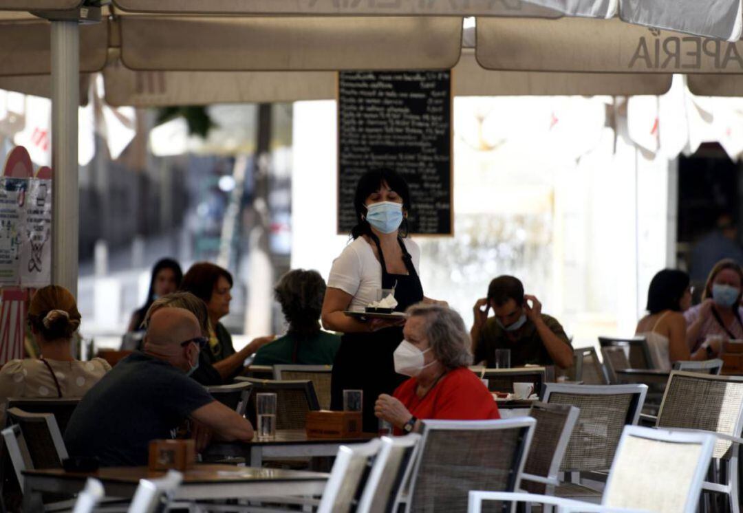 Una camarera con mascarilla atiende a los clientes en una terraza de un bar