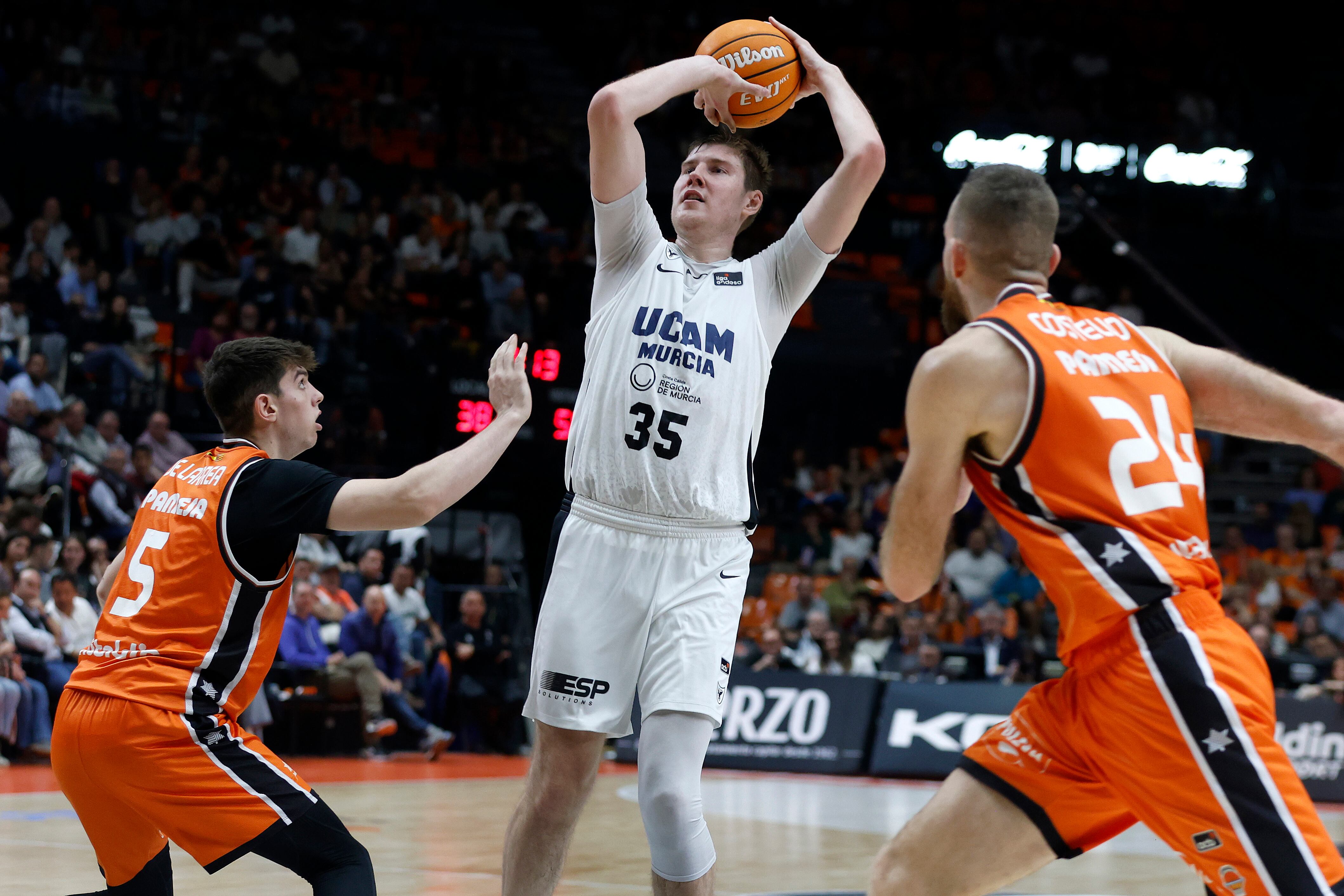 VALENCIA, 05/04/2025. El jugador de UCAM Murcia, Simon Birgander (c), lanza ante los jugadores de Valencia Basket, Sergio de Larrea (i) y Matt Costello, durante el encuentro correspondiente a la fase regular de la Liga Endesa que disputan hoy sábado Valencia Basket y UCAM Murcia en el pabellón de la Fuente de San Luis de Valencia. EFE/Miguel Ángel Polo.