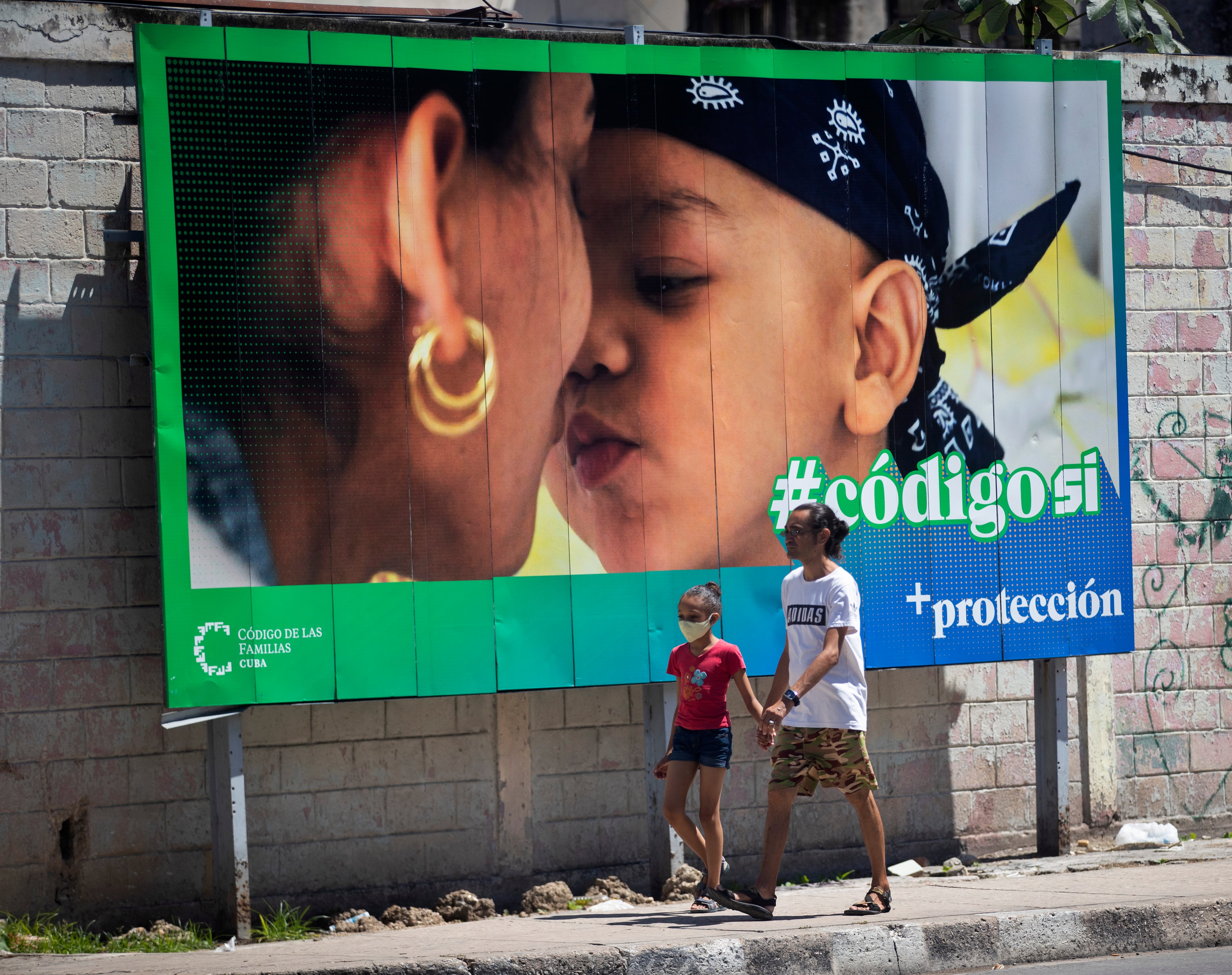 Un hombre y su hija pasan caminando frente a una valla que hace parte de la campaña por el SÍ en el referendo sobre el código de familia en La Habana,