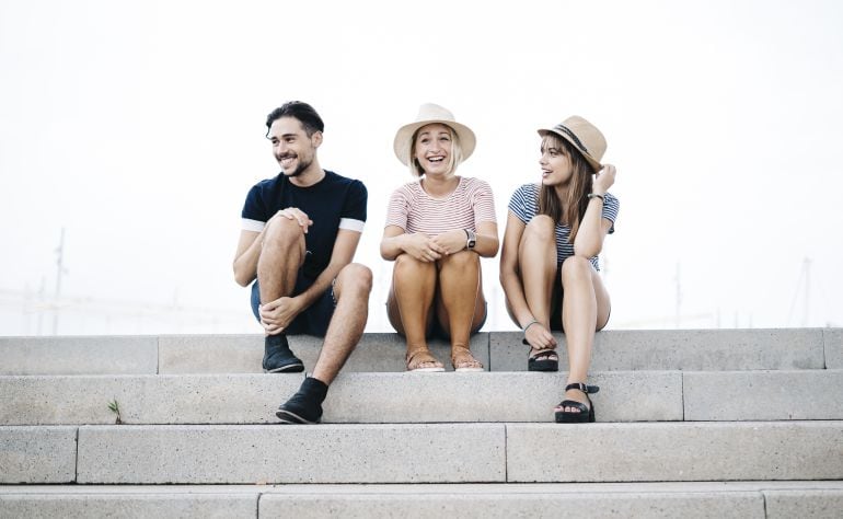 Tres jóvenes sonríen sentados en una escalera.