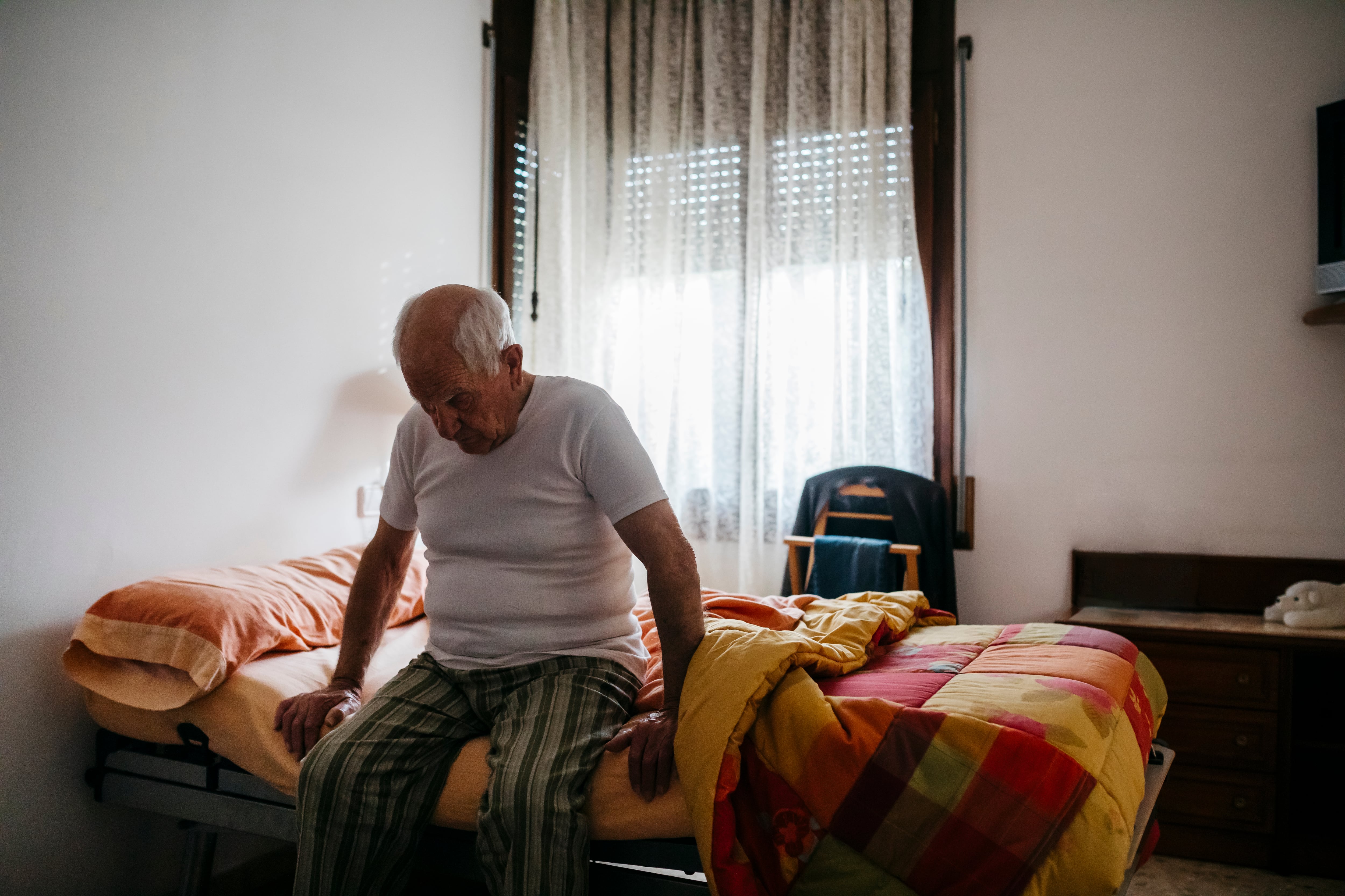 Un anciano, sentado al borde de su cama