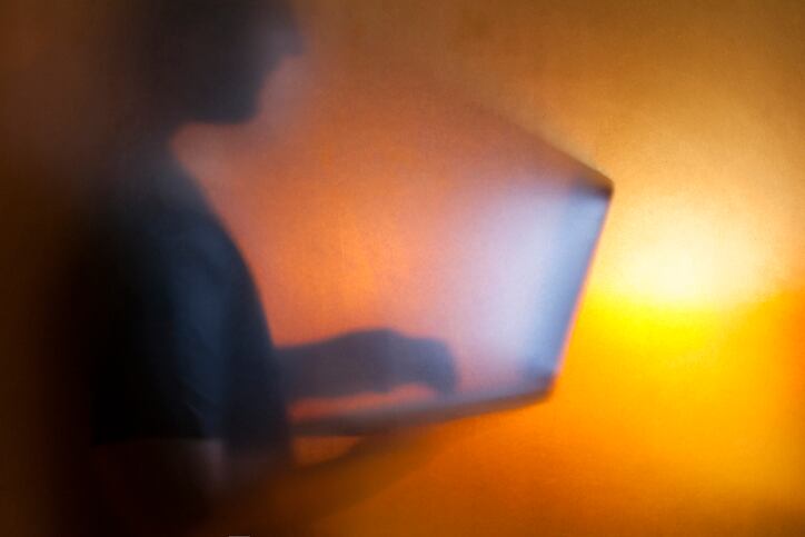 Silhouette of man holding computer with light coming out from screen