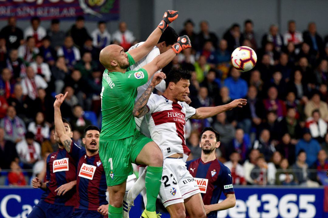 El centrocampista argentino del Huesca Damián Musto salta por el balón con el serbio Marko Dmitrovic, portero del Eibar.