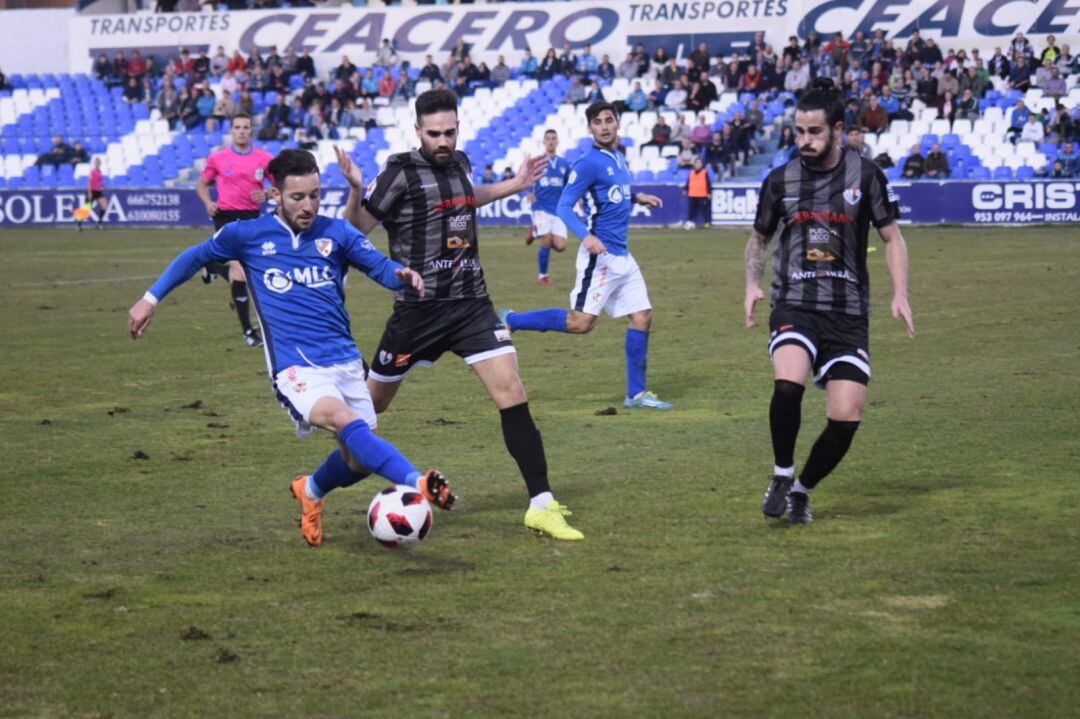 Miguelito conduce el balón ante la presión de dos jugadores del Antequera