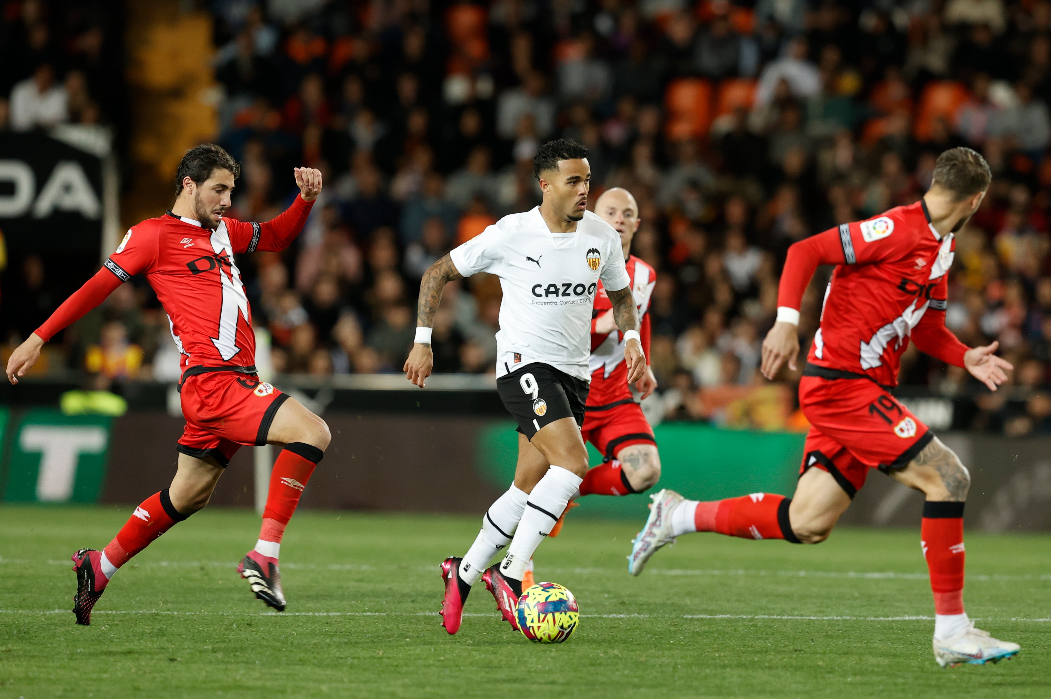 El delantero neerlandés del Valencia, Justin Kluivert (c), conduce el balón ante el centrocampista del Rayo Vallecano, Santi Comesaña (i), durante el encuentro correspondiente a la jornada 27 de primera división que disputan hoy lunes en el estadio de Mestalla, en Valencia. EFE / Kai Forsterling.