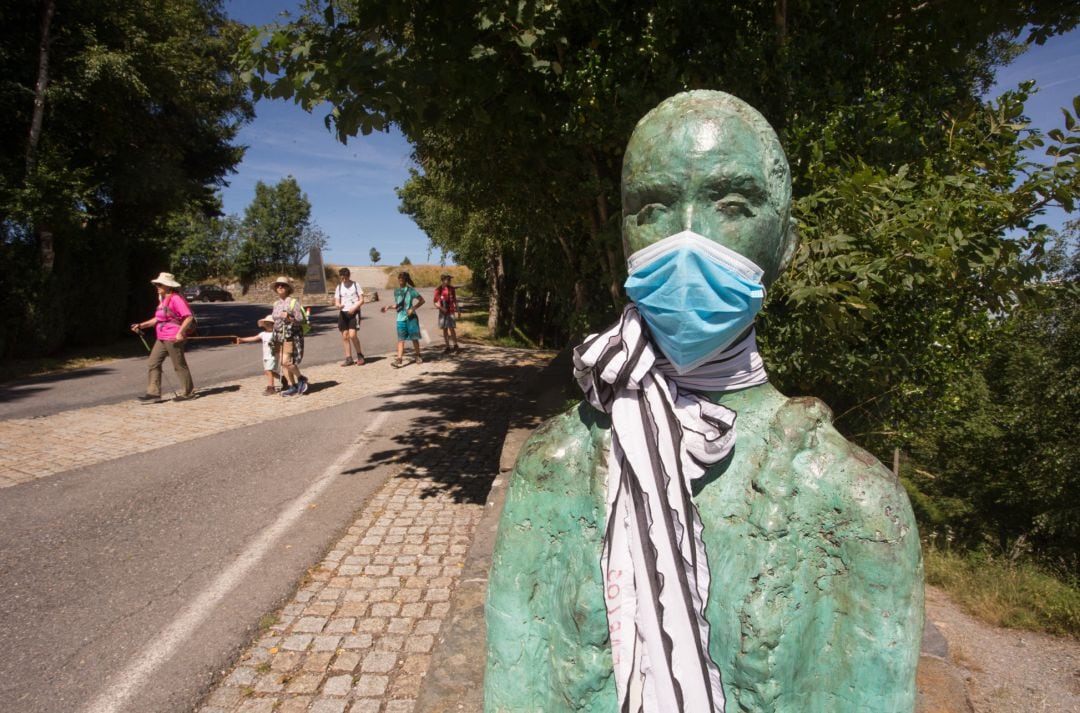 Un grupo de peregrinos llega a O Cebreiro pasando junto a la escultura del coruñés Miguel Couto, que luce desde hace semanas una mascarilla quirúrgica en recuerdo de las víctimas del coronavirus.