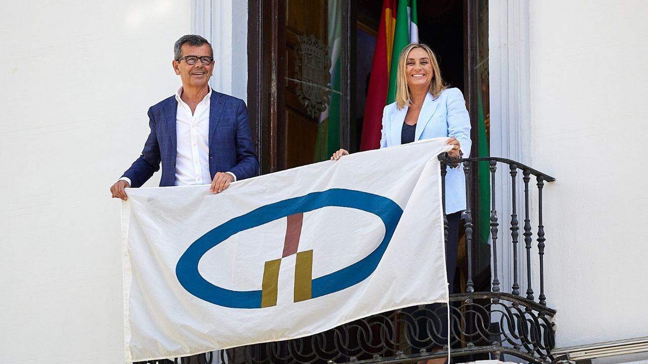 La alcaldesa de Granada, Marifrán Carazo, y el concejal de Cultura, Juan Ramón Ferreira, despliegan en uno de los balcones del ayuntamiento la bandera de las ciudades Patrimonio Mundial