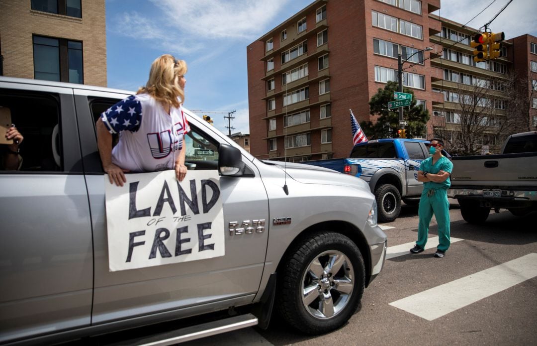 Sanitarios se paran en la calle en protesta contra cientos de personas que desfilaban para exigir que se levante la orden de quedarse en casa en Denver (Colorado).