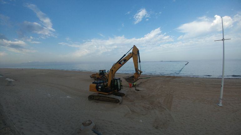 Una máquina se afana en colocar el tubo que conducirá la arena hasta la orilla de la playa de La Victoria en Cádiz