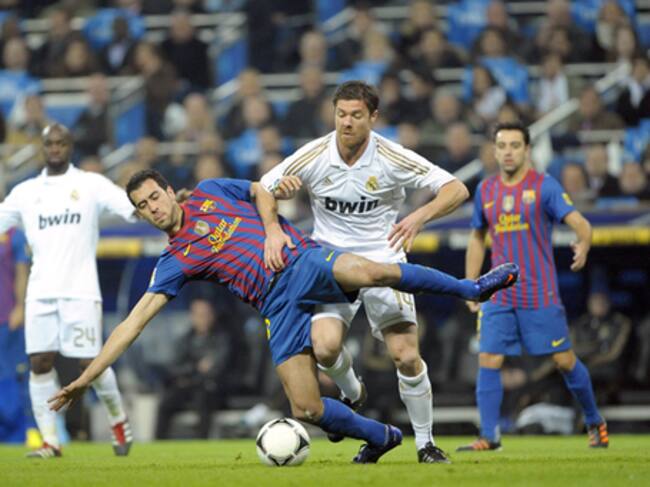 El centrocampista del F. C. Barcelona, Sergio Busquets , cae ante la entrada del jugador del Real Madrid, Xavi Alonso, durante el encuentro correspondiente a la ida de los cuartos de final de la Copa del Rey, que ambos equipos disputan esta noche en el es